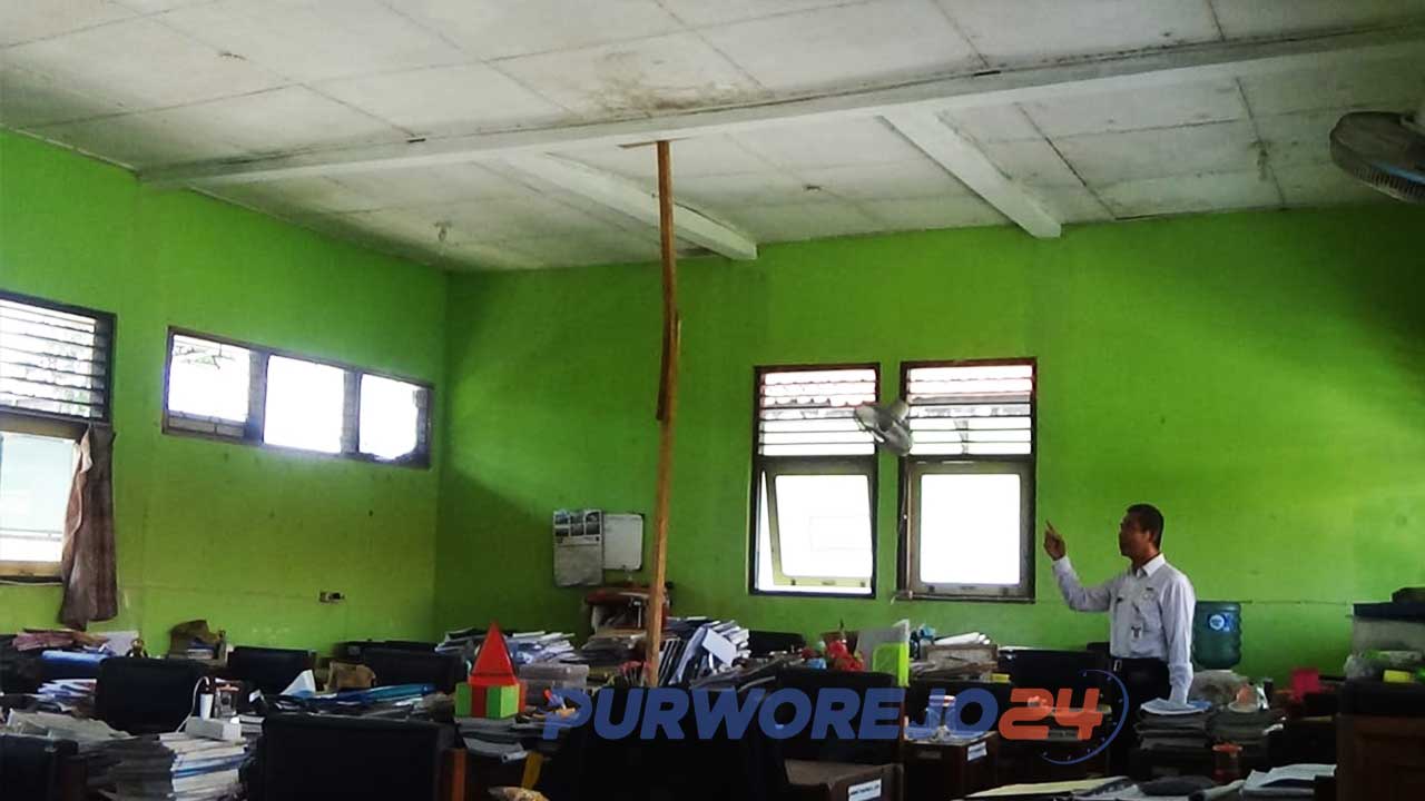 Seorang guru menujukkan atap ruang guru yang disangga batang kayu.
